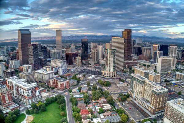 Aerial view of Denver skyline and distant mountains under cloudy skies.